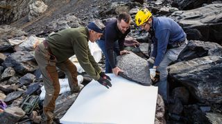 Researchers move a rock imprinted with fossilized animal remains onto a protective white sheet for transportation.